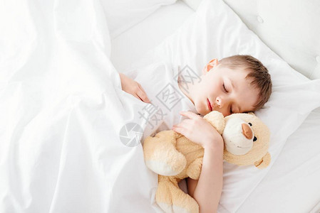 小男孩睡在床上抱着他最爱吃的泰迪熊图片