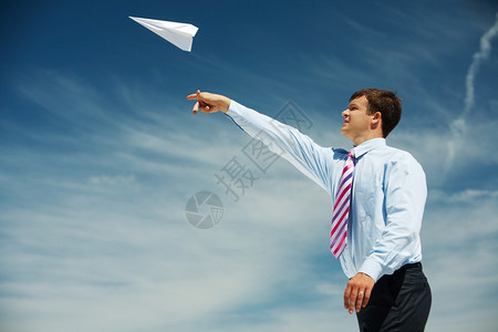 商人让纸飞机翔在蓝天背景下看着它的形象图片