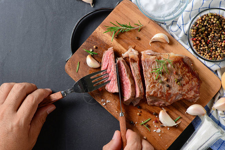 人手切牛肉排食盐大蒜和迷迭香叶在黑图片