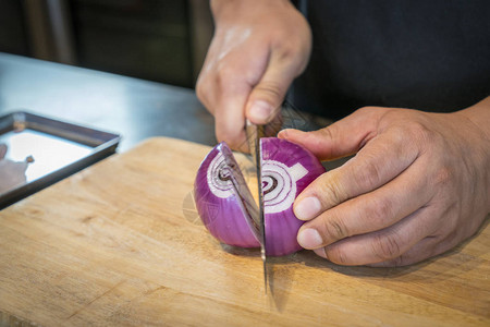 厨师用刀在砧板上切红洋葱图片