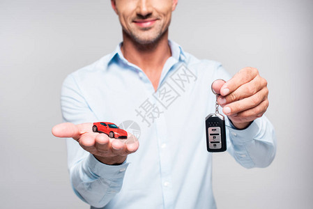 手持汽车警报遥控器和白色被孤立的玩具红色汽车的图片