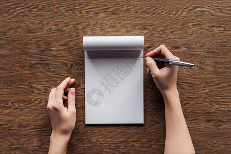持笔者在木制背景的空白笔记本上持有笔的人作图片