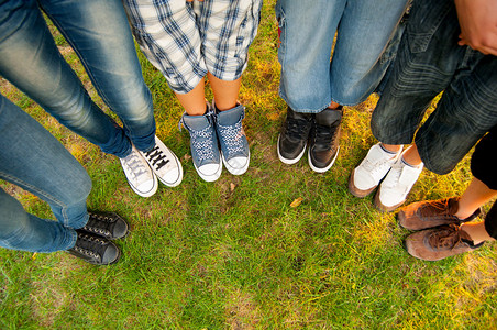 十几岁的男孩和女孩的腿和运动鞋站在草地上半圈图片
