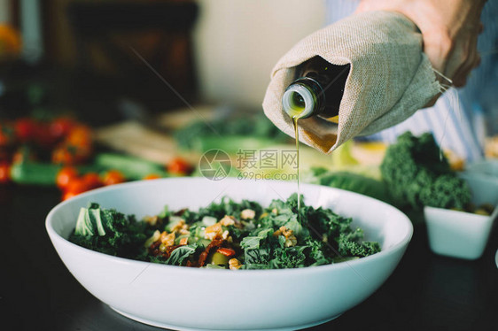 女人往绿色蔬菜沙拉里倒油图片