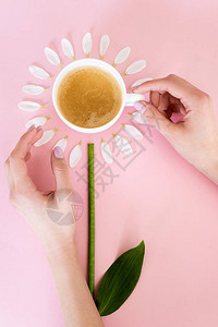 妇女在粉红色的白色花瓣附近触摸咖啡杯的顶视图图片