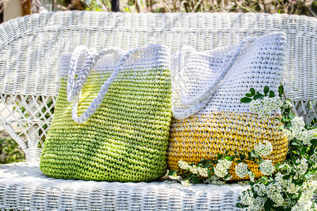 两个黄色绿色和白色的手工编织袋子放在花园的白色柳条沙发上图片