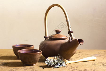 日本棕色粘土茶壶两个茶杯和一个含干茶叶的木背景图片