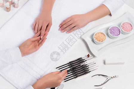 美容师在餐桌上用五颜六色的海盐指甲油指甲钳和美容沙龙修指甲工具给女人图片