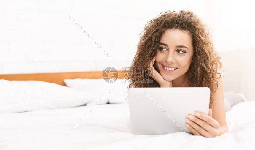 带着数字平板电脑躺在床上神秘地微笑和寻找复制空间的图片