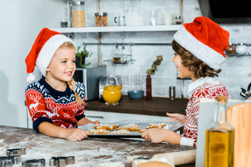 穿着圣诞帽子的可爱快乐孩子拿着姜饼干烤盘图片
