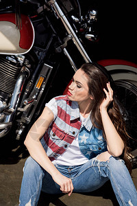 穿着戴尼姆背心的时髦年轻黑发美女坐在摩托背景图片