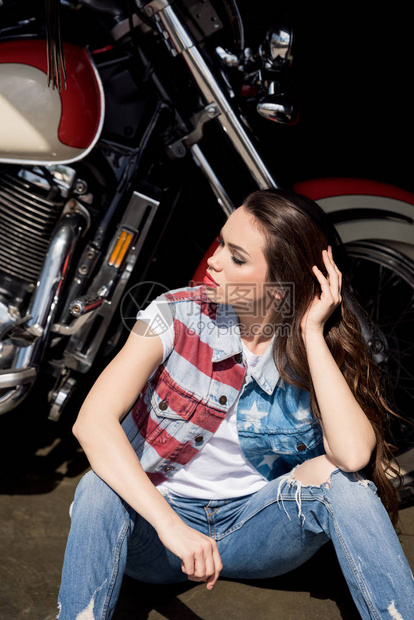 穿着戴尼姆背心的时髦年轻黑发美女坐在摩托图片
