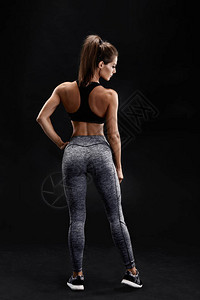 一个穿着运动服腹部肌肉发达的女强人的镜头摆在黑色背景上的健身女模特一个女人背着她站背景图片