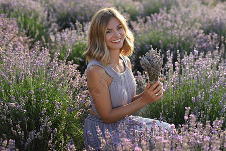 在紫衣草田里拿着鲜花看着摄影机的背景图片