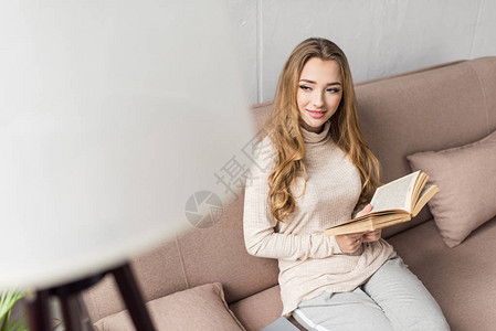 快乐的年轻女子有书在舒适的沙发图片