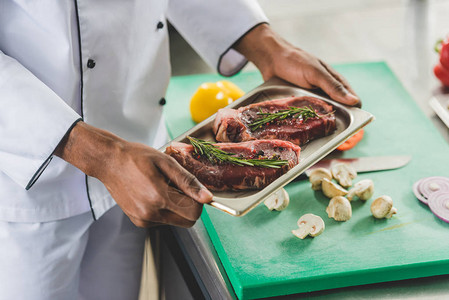 非洲人厨师在餐厅厨房用生肉端着餐盘的图片