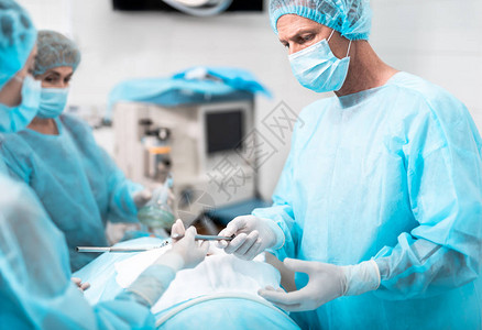 中年医生戴防护面罩手持腹腔镜工具站在手术室与背景图片