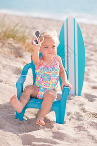 一个岁大的女婴坐在沙滩上的小沙滩椅上她拿着太阳图片