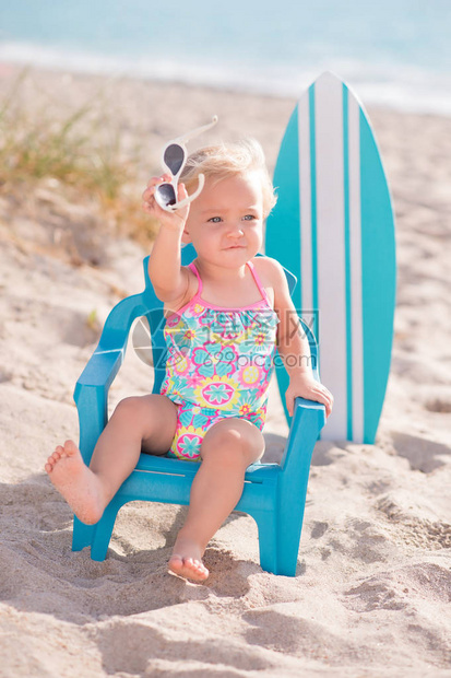 一个岁大的女婴坐在沙滩上的小沙滩椅上她拿着太阳图片