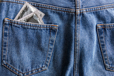 蓝色牛仔裤口袋里的一对银色避孕套背景图片