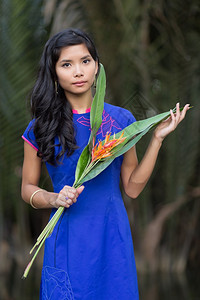 穿蓝AoDai礼服的年轻漂亮的越南女人拿着大叶子的橙背景图片