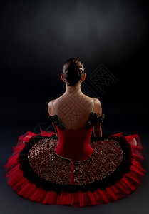 深色背景上坐着的芭蕾舞女演员的背影图片