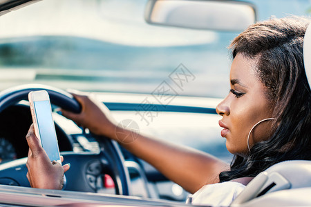 年轻女驾驶员开车时用智能手机打字图片