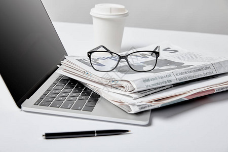 白色商业报纸眼镜笔和纸杯附近空白屏幕的膝上型计算图片