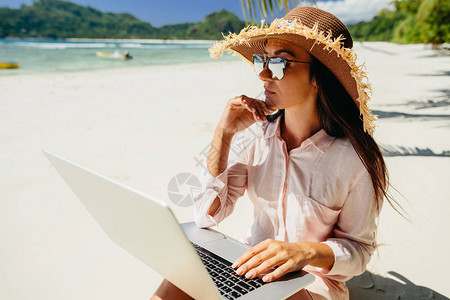 热带海滩上的女自由职业者通过互联网在笔记本电脑上远程工作旅行时工作图片