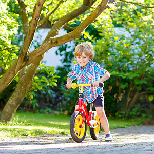 活跃的金发小男孩穿着五颜六色的衣服在国内花园里驾驶自行车图片