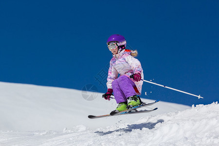小女孩滑雪者在跳跃中翱翔在斜坡上图片