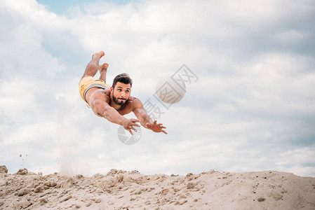 英俊的年轻人一边打沙滩排球一边跳球图片