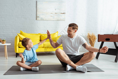 快乐的父亲和儿子在坐露的健身垫子上图片