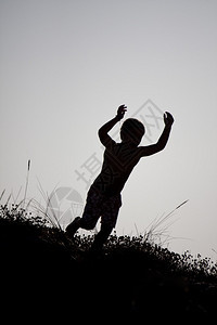 一个小男孩从沙丘上跳下来的剪影背景图片