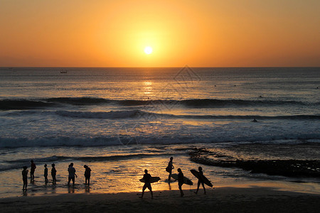 三个冲浪者剪影在红色日落的巴厘岛库塔海滩印度尼西亚背景图片