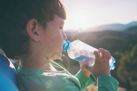 一个孩子从瓶子里喝水男孩解渴了孩子正在山间旅行疲倦的孩子图片