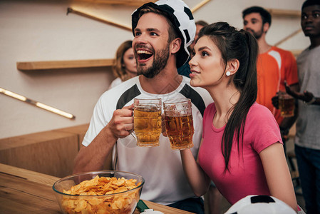 戴着足球帽的兴奋男人和女朋友碰杯啤酒背景图片