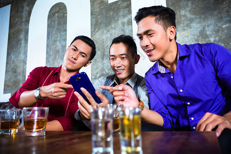 亚洲年轻和英俊的党员团体或男朋友在花哨夜总会里观看智能手机背景图片