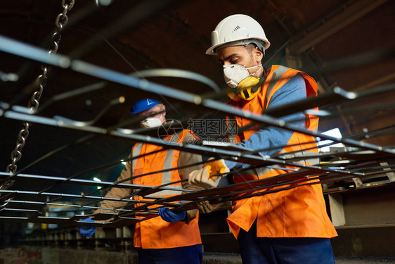 低角度观察身穿反射背心和硬件举重金属板的钢铁厂工人在起重机帮助下图片