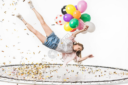 女孩抱着多彩气球坠落在蹦床上图片