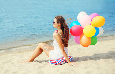 美丽的年轻美女带着多彩的气球坐在沙图片