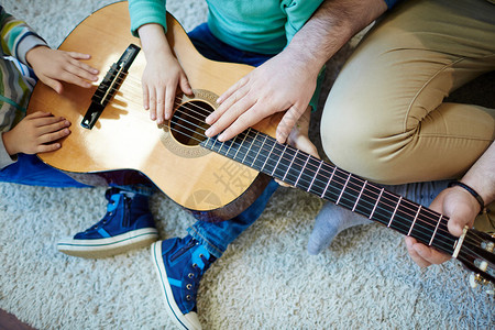 男人和他的儿子在吉他弦上的手图片