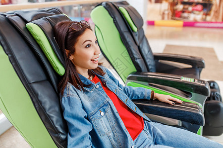 年轻女士在商场自动按摩椅上购物图片