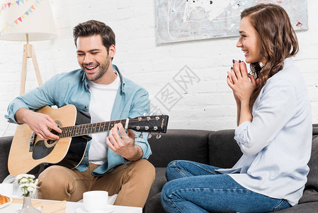 坐在沙发上的女人听男人唱歌的男子在家里用图片