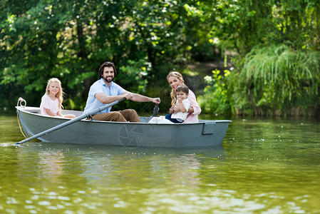 快乐的年轻家庭在公园河边的船上共渡时图片