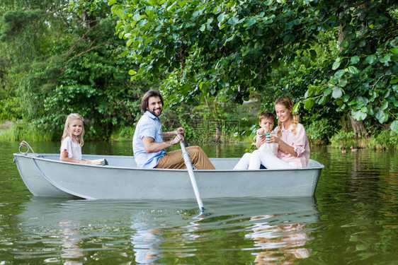笑的年轻家庭在公园湖边小船上共渡时图片