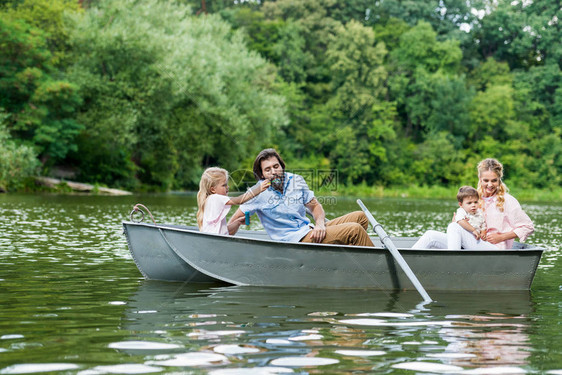 美丽的年轻家庭在公园湖边的船上共渡时图片