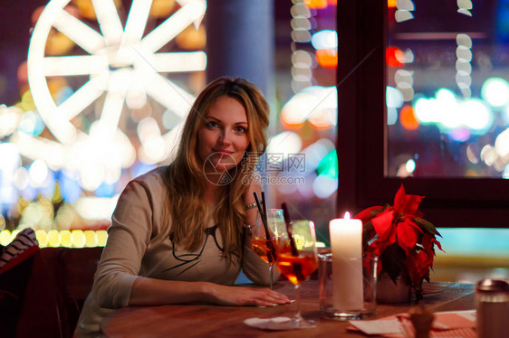 年轻漂亮的女人在法国巴黎的一家室内咖啡馆和餐厅喝香槟鸡尾酒圣诞市场与摩天轮和灯晚上做图片