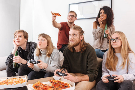 坐在沙发上一起玩电子游戏吃披萨在家喝啤酒时共度时间的一群朋友图片