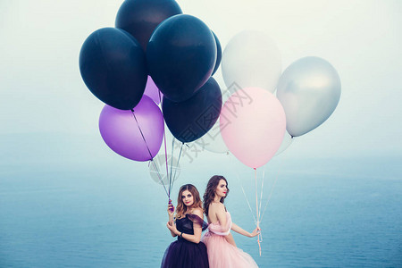 两个年轻时尚的女穿着装扮着拿气球对抗天空图片